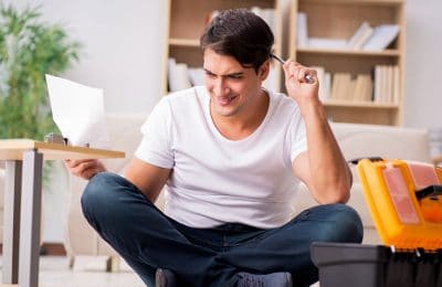 A confused man holding tools and instructions booklet