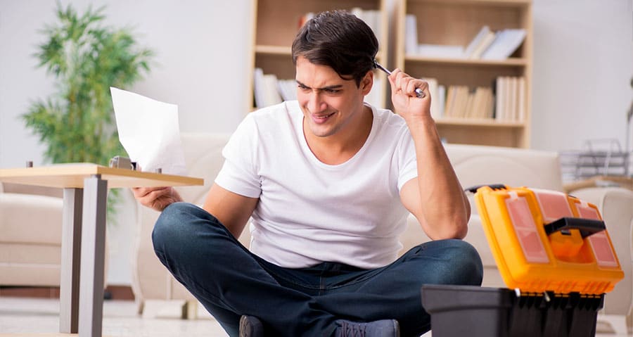 A confused man holding tools and instructions booklet